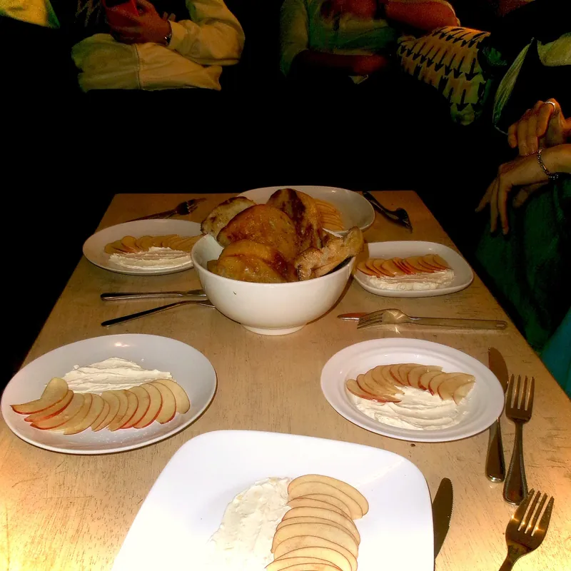 The table at night, set with plates of thinly sliced apple fanned over cream around a bowl of pastries.