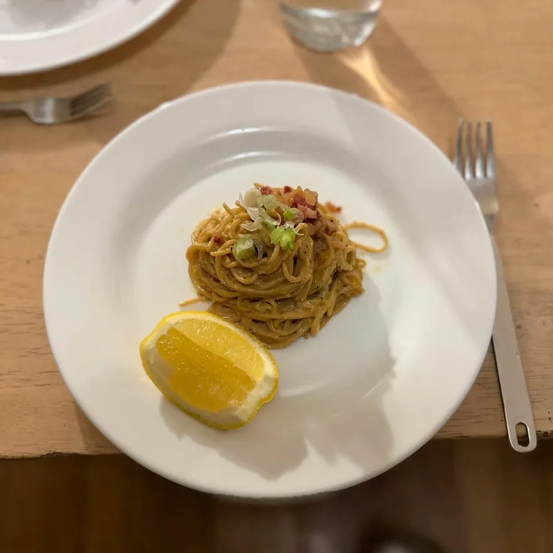 A nest of spaghetti with herbs and chili, a lemon wedge beside it, on a white plate.