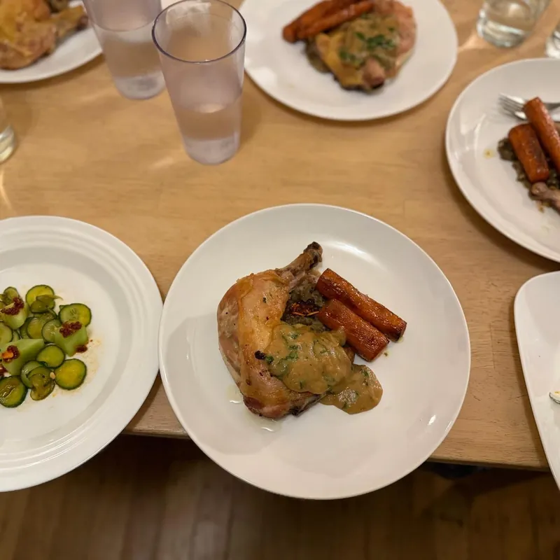 Overhead view of the table: plates of the chicken with carrots and the cucumber salad, glasses of water between them.