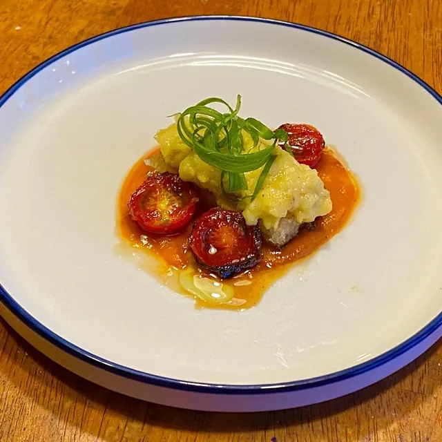 Tomato and egg, plated small: blistered cherry tomatoes in sauce under a mound of soft scrambled egg with scallion curls, in a blue-rimmed bowl.